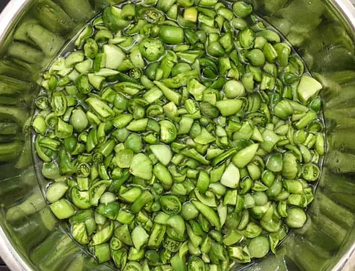 A huge metal bowl of green tomatoes, cut into chunks, sugared, and macerated for 24 hours in the fridge. Instead of plastic, use glass or metal bowls for cooking and food prep, especially when using acidic foods, since compounds in plastic can leach into your food.